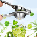 Espremedor manual de limão em aço inoxidável extraindo suco de limão em um copo com frutas cítricas ao redor.
