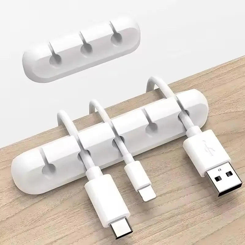 Organizador de cabos adesivo em silicone branco fixado na mesa segurando cabos USB, Lightning e USB-C organizados.