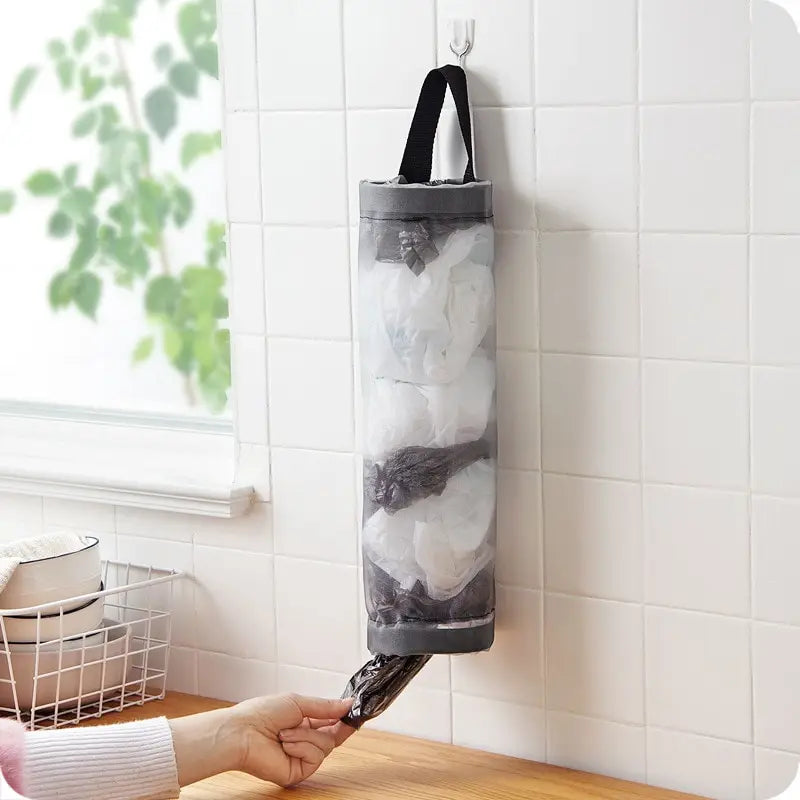 Suporte organizador de sacolas plásticas pendurado na parede da cozinha, com abertura inferior para retirar as sacolas com praticidade.